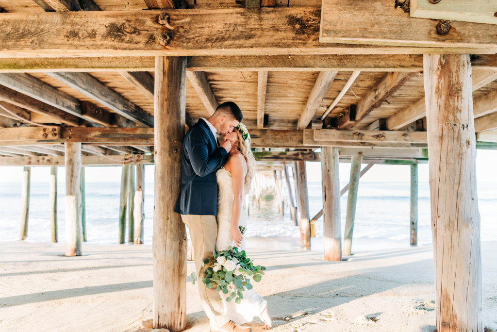 bride and groom kissing under pier