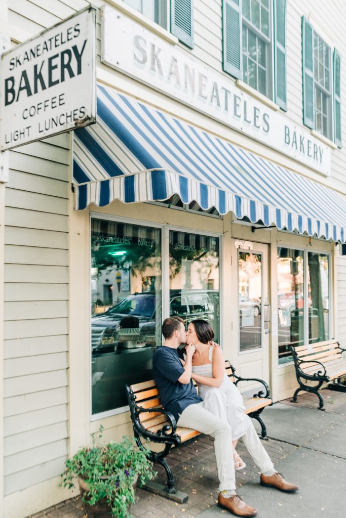 couple snuggling on bench infront of Skaneateles Bakery