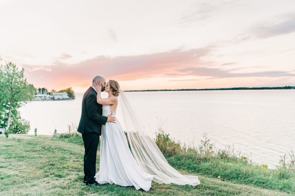 bride and groom kissing at sunset over looking Sackets Harbor