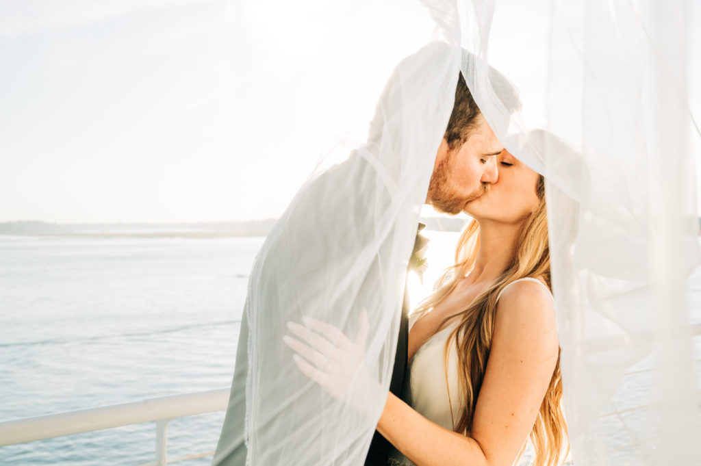Bride and groom kissing under her veil at sunset
