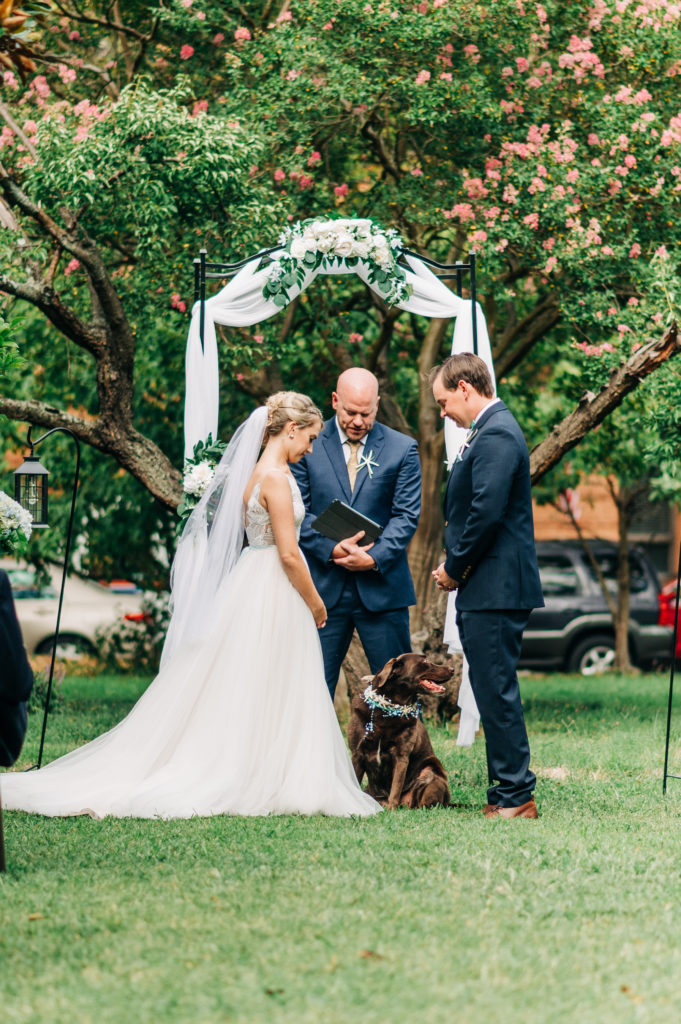 Bride, groom, VA Beach officiant, and dog bowing head during ceremony
