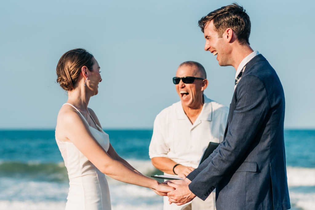 OBX officiant, bride and groom laughing during ceremony on the beach