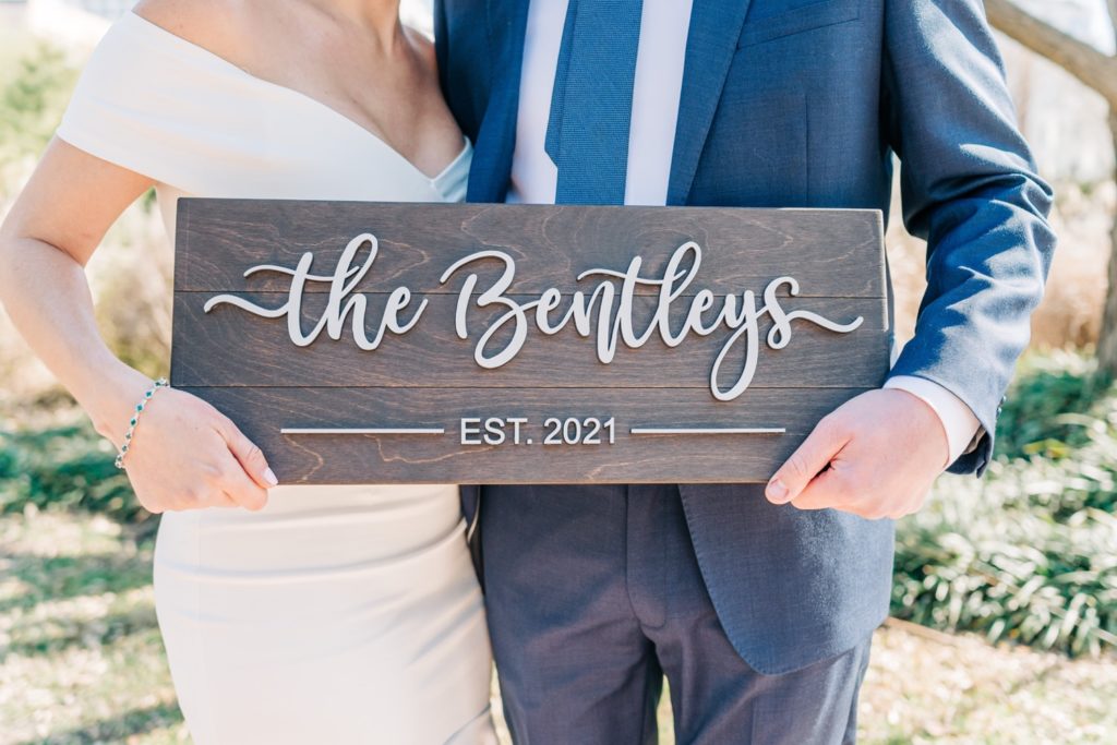 Bride and groom holding wood sign with their last name