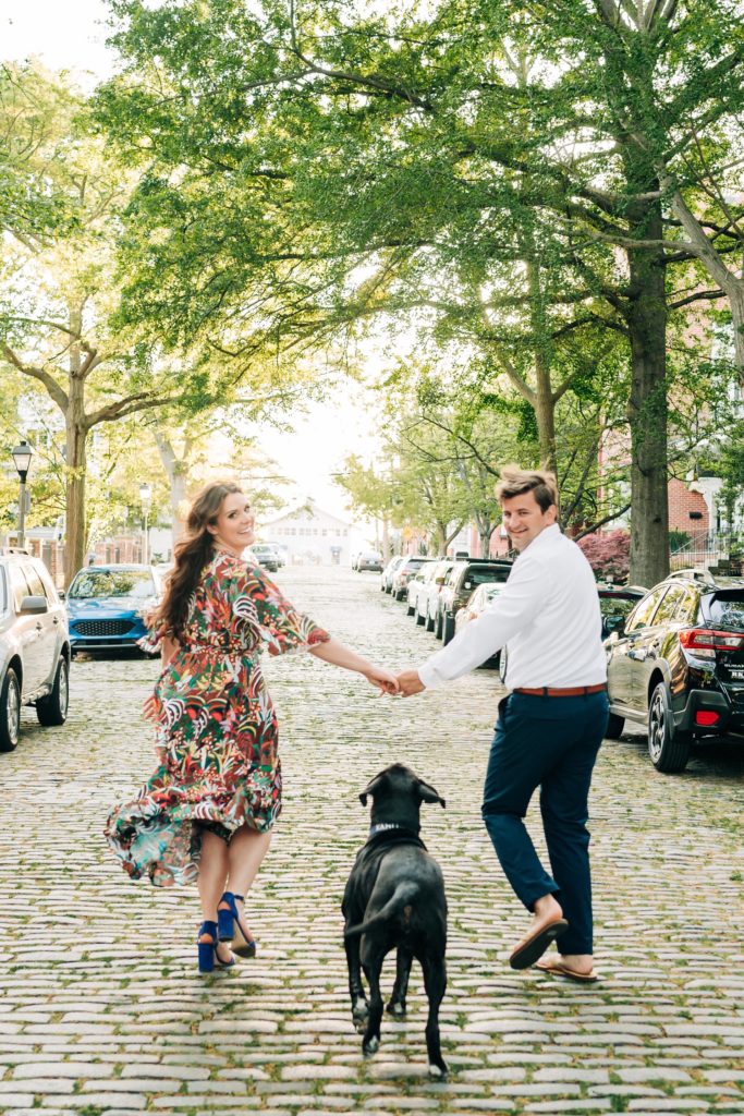 Couple looking back at their dog and holding hands while walking down the street