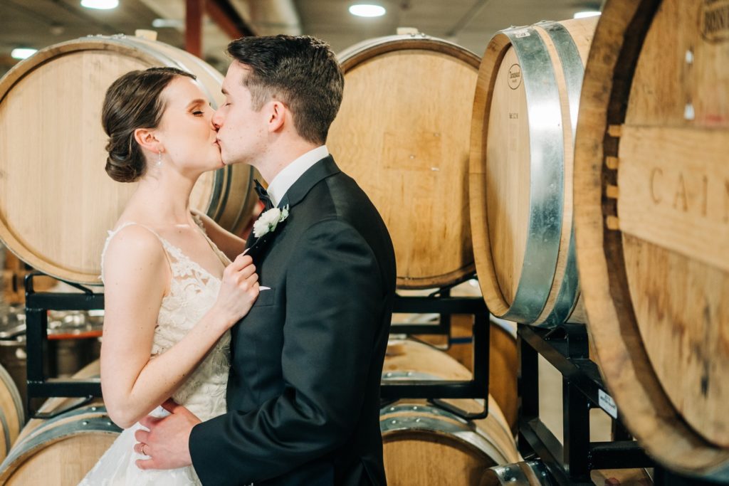 bride and groom kissing infant of wine barrels at Windridge Vineyards