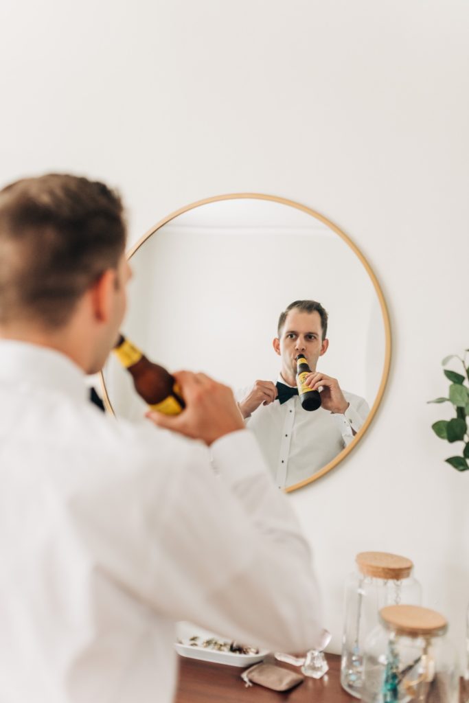 Groom drinking a beer and looking into a mirrior before wedding ceremony