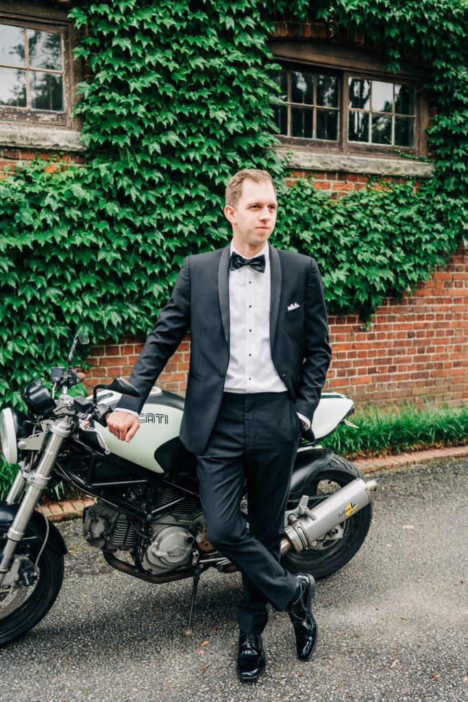 Groom leaning up against his black and white motorcycle