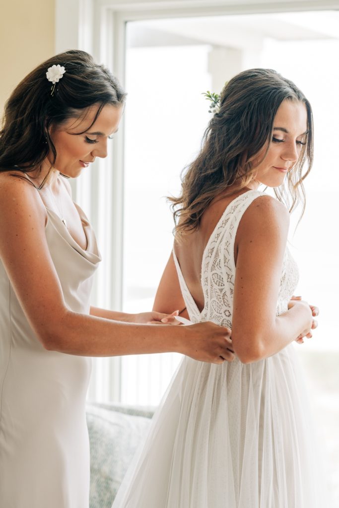 Bride getting dressed with help of bridesmaid at Hatteras OBX wedding