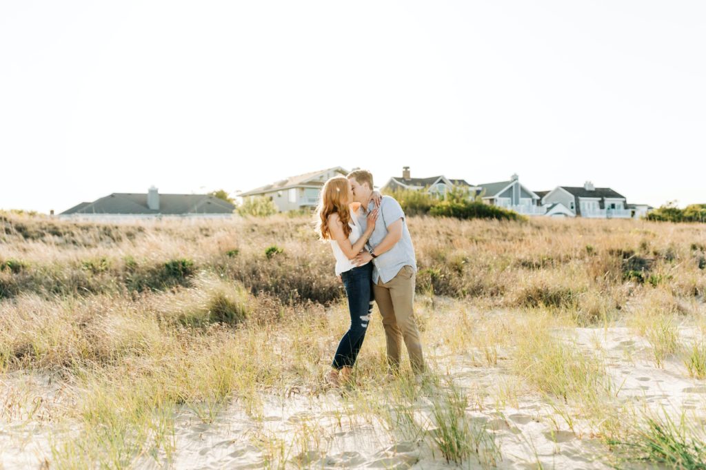 engaged couple kissing each other while embracing in front of houses on the beach at a Virginia state park 
