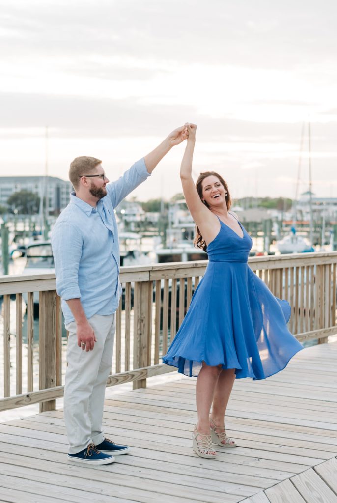 engaged man twirling his fiancée on the pier while she wears a blue dress in the summer