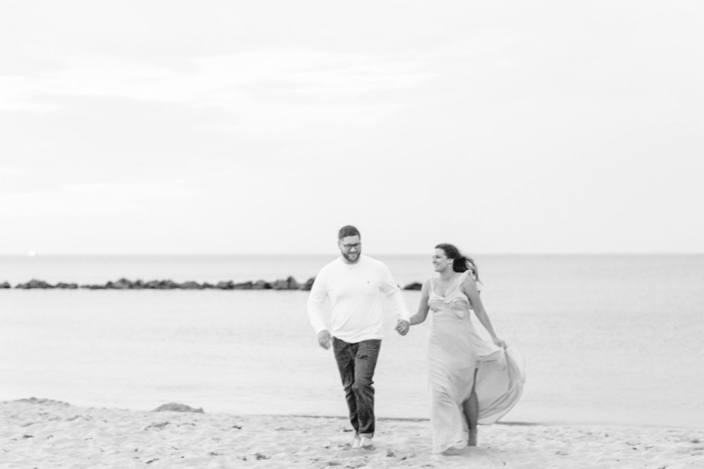 black and white photo of an engaged couple running on the beach during sunset for their engagement photos 