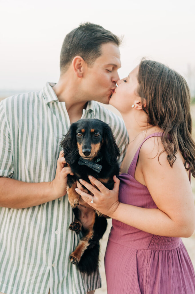 Couple kissing in Virgina Beach holding their daschund dog