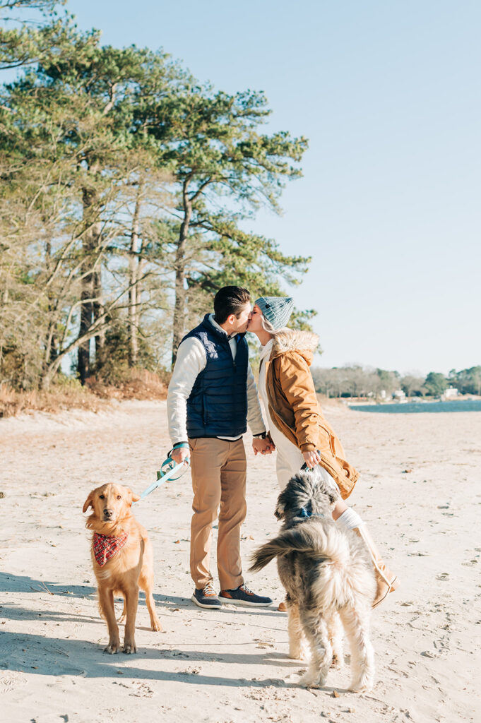 couple kissing on the beach while walking their dogs